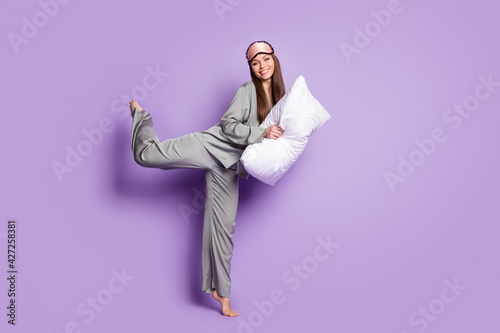 Full length body size view of lovely cheery girl wear pajama holding pillow jumping posing having fun isolated on violet purple color background