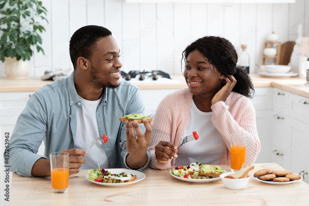 Young Black Affectionate Couple Eating Tasty Food And Chatting In Kitchen