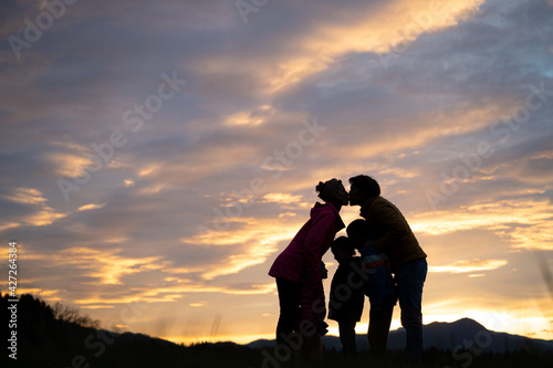 Silhouette of family standing under evening sky with parents giving each other a kiss
