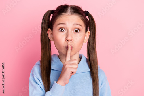 Photo portrait of small schoolgirl put finger near lips staring keeping secret isolated on pastel pink color background photo
