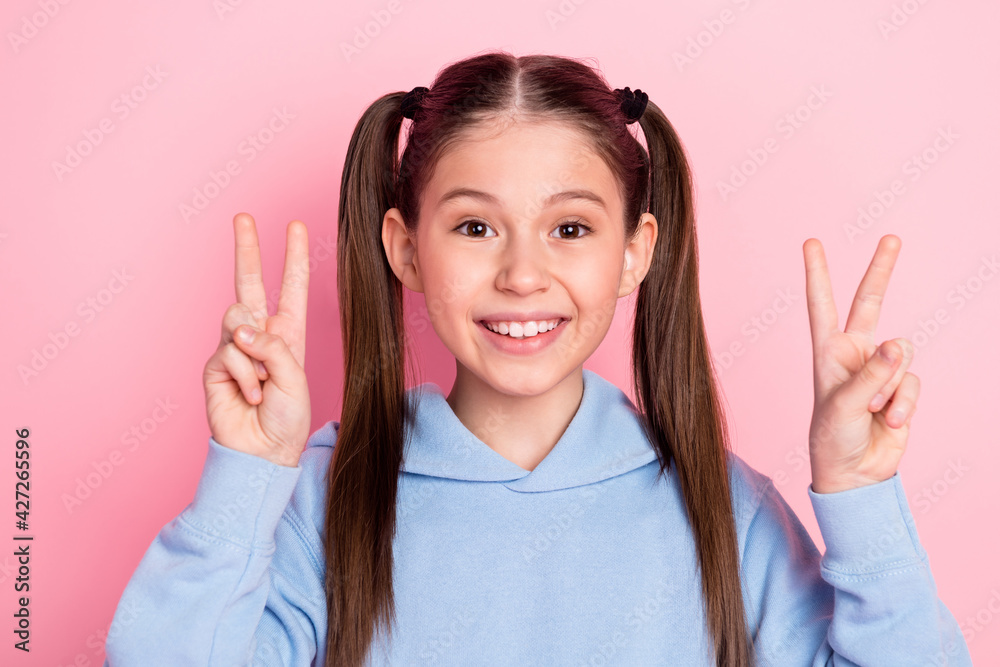 Photo portrait of schoolgirl showing v-sign gesture smiling isolated on pastel pink color background Photo portrait of schoolgirl showing v-sign gesture smiling isolated on pastel pink color background
