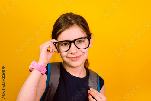Girl kid glasses with smartwatch looking at camera in isolation on a yellow background. Back to school.