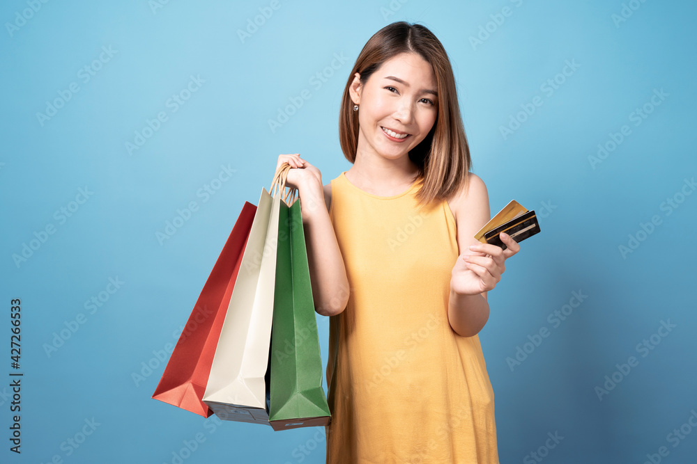 Young asian woman carrying shopping bags and credit card, Isolated on blue background. Young asian woman carrying shopping bags and credit card, Isolated on blue background.