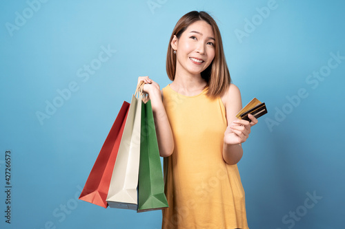 Young asian woman carrying shopping bags and credit card, Isolated on blue background.
