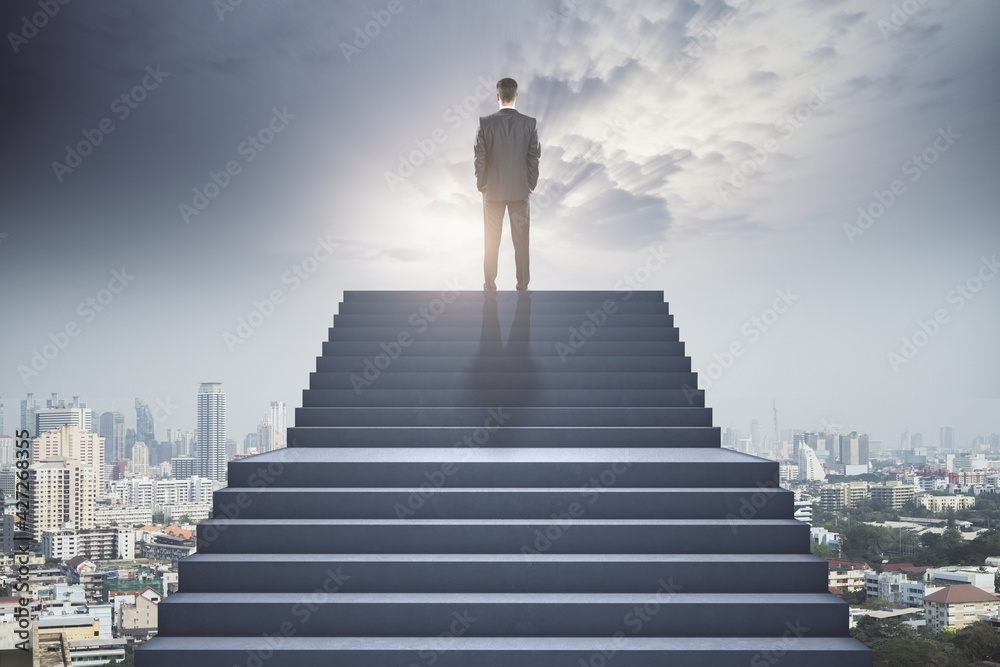 Businessman standing at the top of the concrete stairway watching on the town. Future success and leadership concept Businessman standing at the top of the concrete stairway watching on the town. Future success and leadership concept