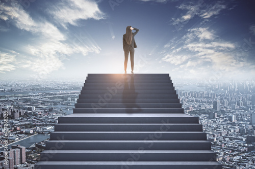 Businesswoman standing at the top of the concrete stairs thinking above the city. Future success and growth concept
