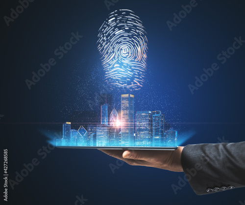 Hand with a tablet holding a city view hologram on a blue background. Internatonal business and market concept photo