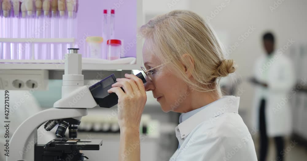 Caucasian mature female scientist looking under microscope analyzing sample. Caucasian mature female scientist looking under microscope analyzing sample.
