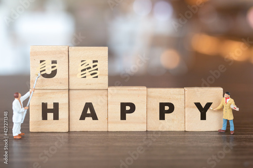 Miniature  people worker team on Unhappy word in wooden alphabet letters with prefix un crossed out, leaving the word Happy