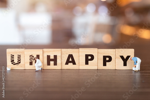 Miniature people worker team on Unhappy word in wooden alphabet letters with prefix un crossed out, leaving the word Happy