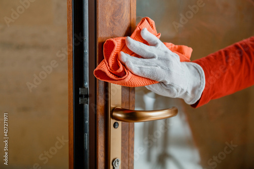 Cleaning front door handle by antibacterial alcohol detergent. Woman Houseworker in white gloves clean Door knob by cloth rag. New normal Covid 19 coronavirus in Surfaces disinfection.