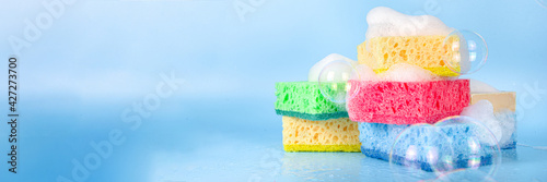 Spring home cleaning, housekeeping concept, Set of various bright detergent washing rubber sponges for cleaning, with lush foam and soap bubbles on a blue background top view copy space photo