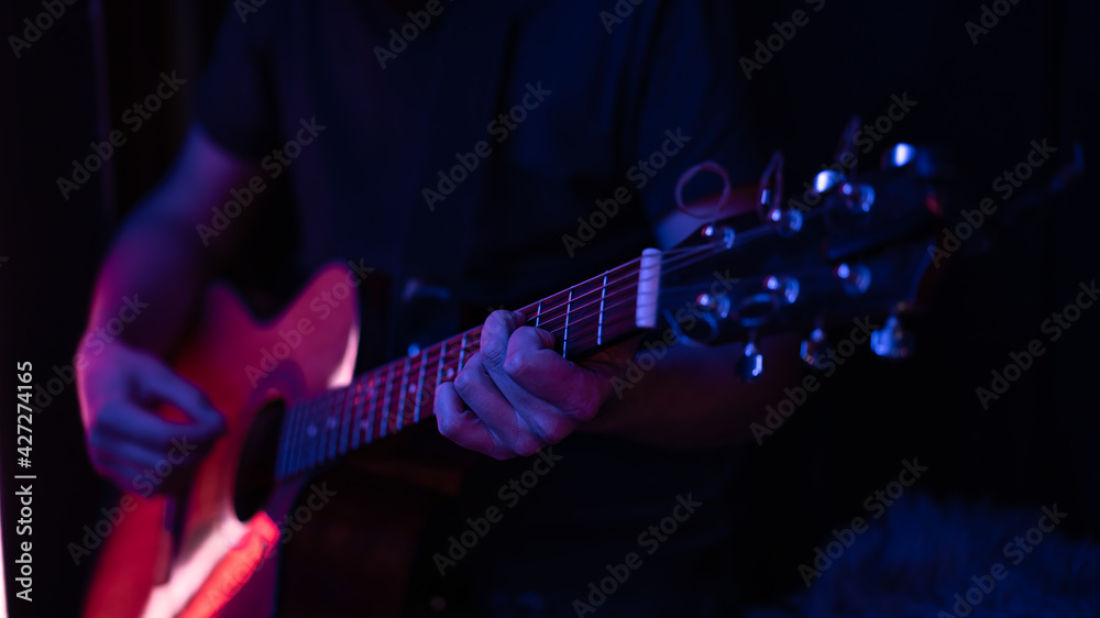 Naklejka premium Close up of a guitarist playing an acoustic guitar in colored lighting.