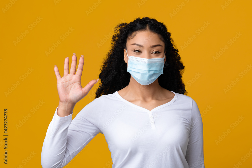 Communication During Coronavirus. Black Lady In Medical Mask Waving Hand At Camera