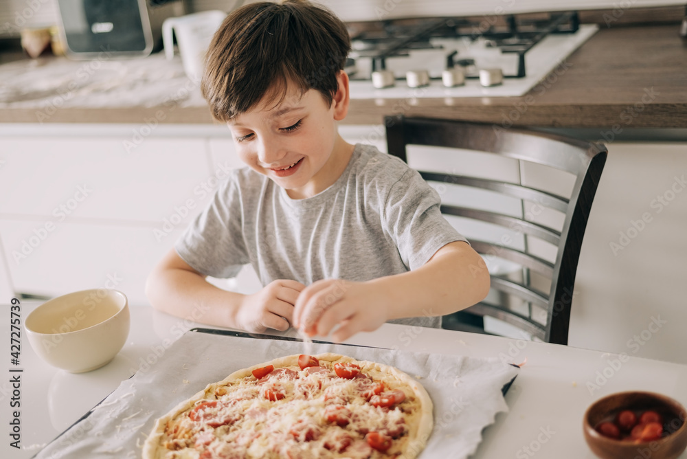 Little kid boy making pizza sitting at the table on the kitchen. Children helping in cooking lifestyle image Little kid boy making pizza sitting at the table on the kitchen. Children helping in cooking lifestyle image