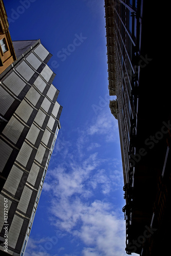 Imagen de ángulo bajo que marca el contraste entre las fachadas de dos edificios, uno moderno y otro antiguo, dejando ver en medio el azul del cielo