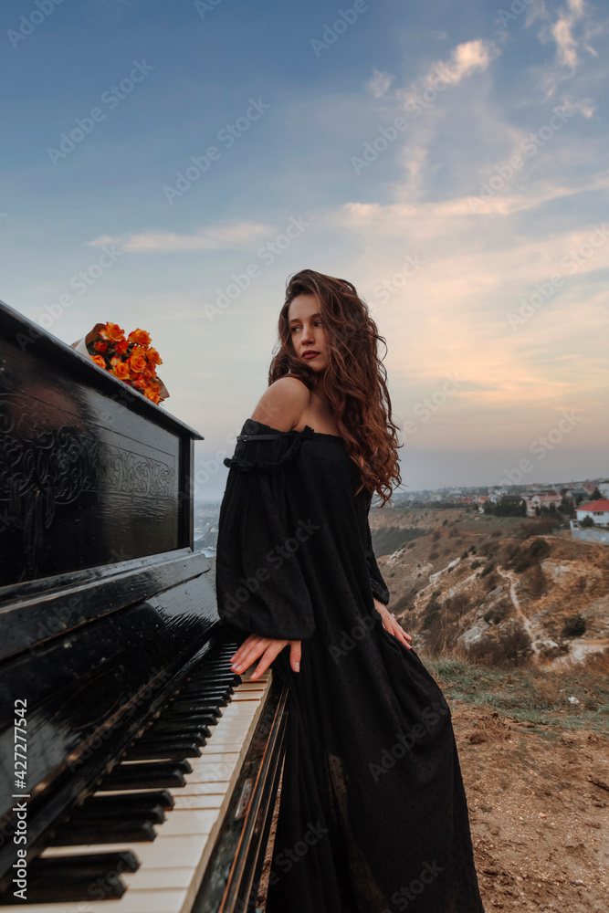 Φωτογραφία beautiful young girl stands near the piano on the background of the sea, the con