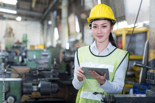 Engineers female and skilled technicians are maintaining machinery. Professional technicians are holding a tablet to control work in industrial plants.