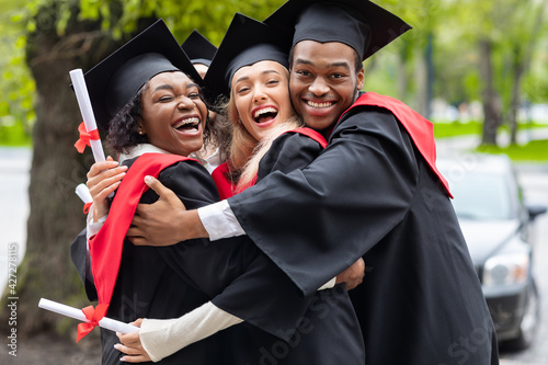 Fototapete Black guy and two young ladies in graduation costumes