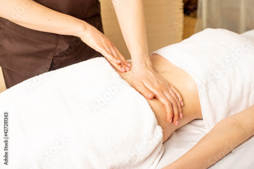 Close up hands of chiropractor or masseur making relaxing massage of stomach for lying woman in clinic interior. Professional woman doctor masseur during work with patient