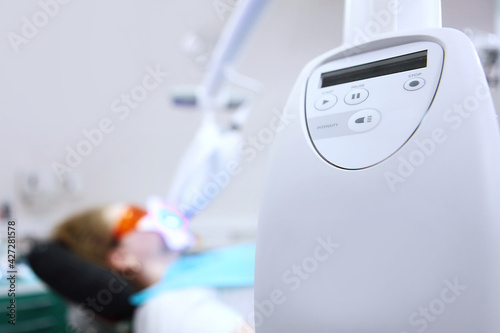 A device for bleaching tooth enamel with cold light.Dental clinic.A young woman whitens her teeth with special equipment.Vertical photo. Cosmetic procedure. The person is out of focus.