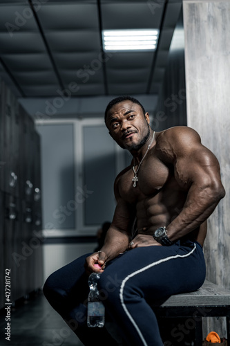Muscular man african bodybuilder. Happy young african man drinking water after exercise.