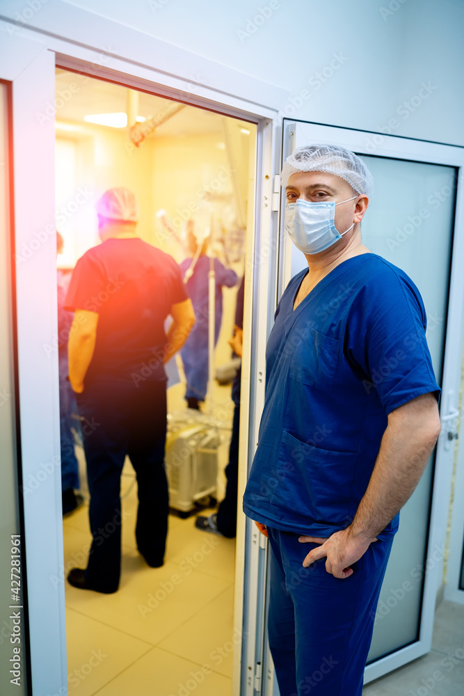 Adult doctor surgeon standing near operating room with other workers in hospital. Adult doctor surgeon standing near operating room with other workers in hospital.