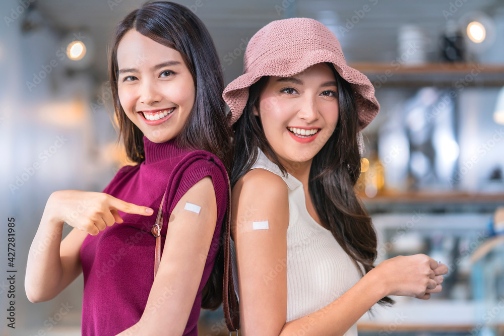 Asian female traveller friends cheerful smiling teenager hand gesture point show vaccine brand against covid-19 with  happiness healthy after getting vaccine prevent
