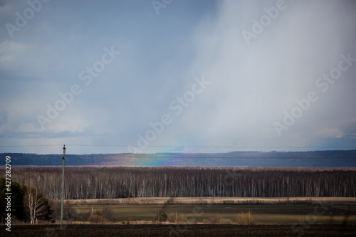 a piece of rainbow against the background of thunderclouds and spring fields