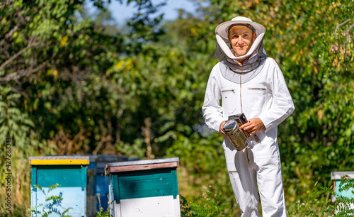 Man examining hives in summer. Agricultural beekeeper in protective cloth posing for camera.