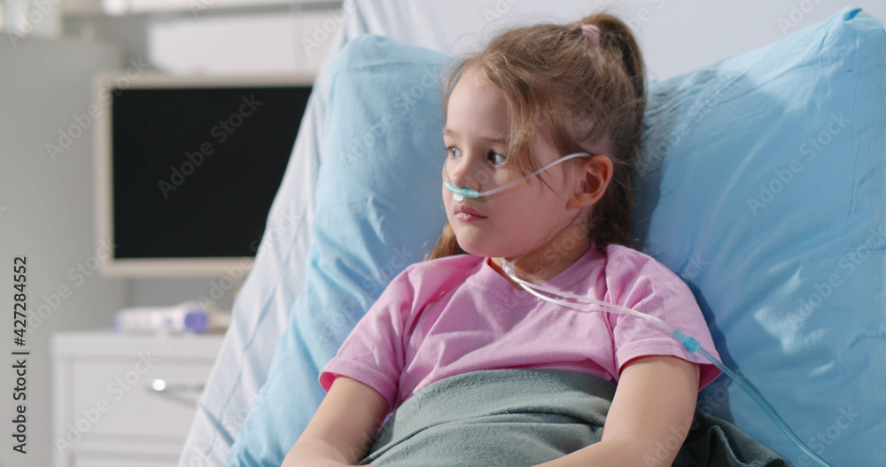 Girl suffering from pneumonia lying in hospital bed with oxygen nasal