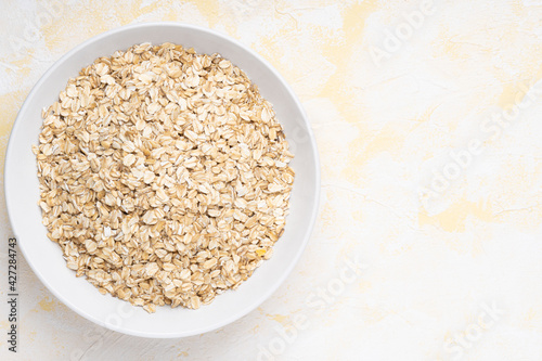 Oat flakes in a white plate on a yellow cement background © Svitlana