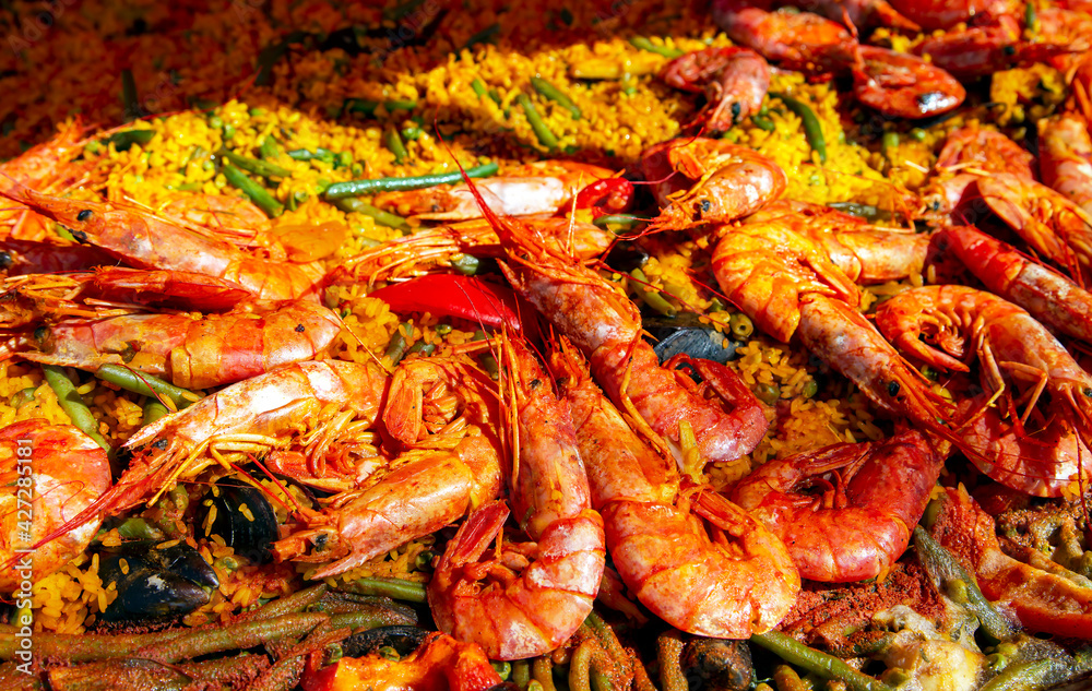 Spanish paella with green beans, large prawns and other seafood cooked in a wok pan on the street. 