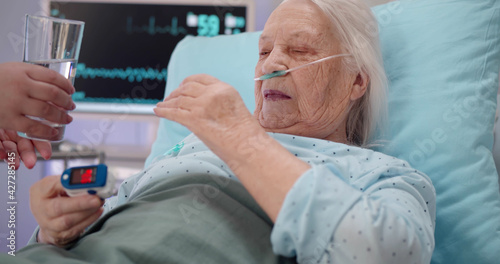 Close up of nurse giving medicine to aged female patient in hospital bed