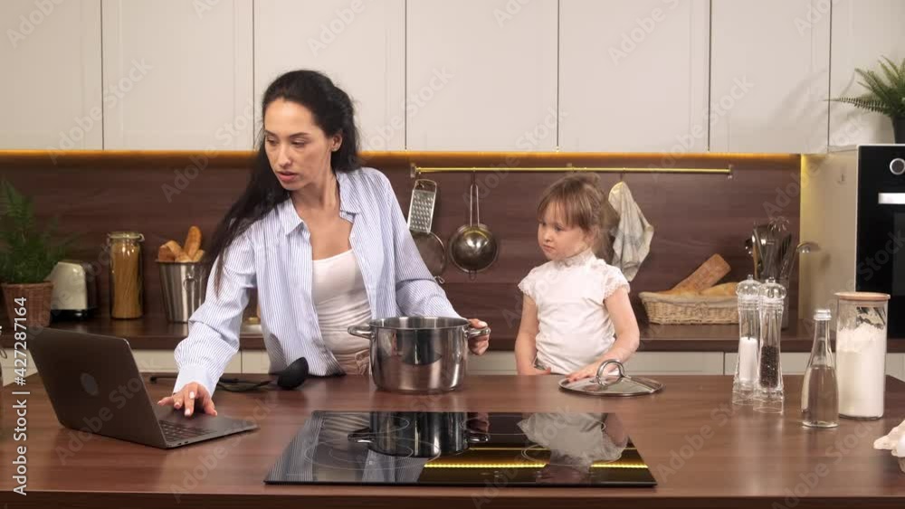 Attractive mother and her daughter cook in the kitchen looking recipe in a laptop. Single mom spends time with her baby Attractive mother and her daughter cook in the kitchen looking recipe in a laptop. Single mom spends time with her baby