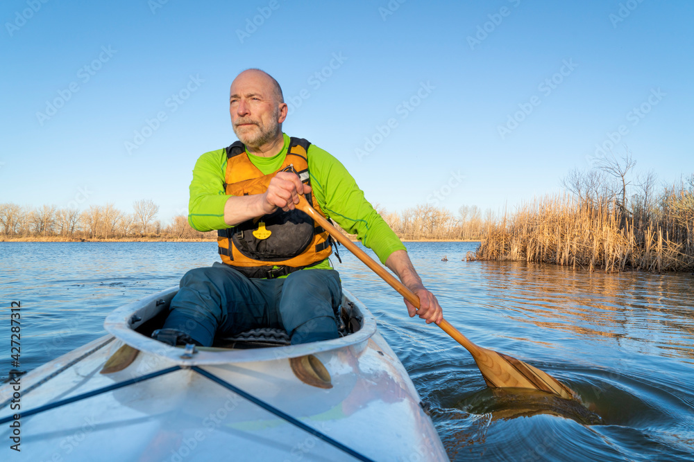 senior male is paddling expedition canoe, early spring scenery on a lake in northern Colorado, POV from boat bow