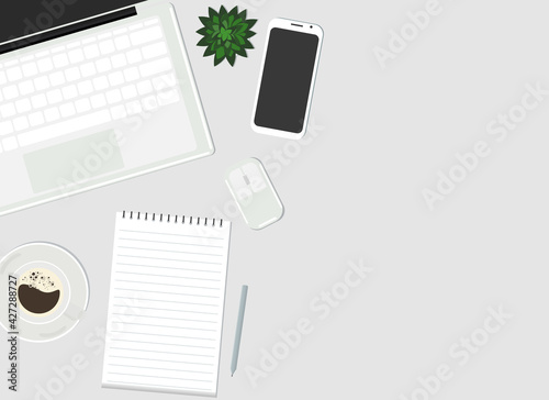 On the desktop are a laptop, a mobile phone, a plant, a cup of coffee and a paper notebook. View from above