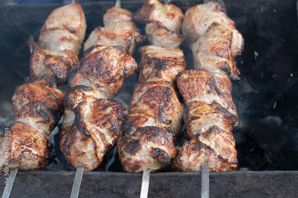 An appetizing barbecue of marinated meat with spices on skewers is fried on hot coals on the grill. Horizontal photo close-up. Food concept. Selective focus. 