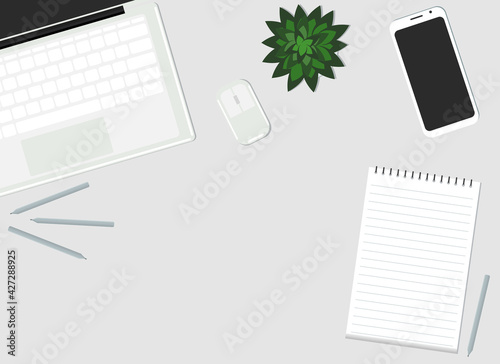 On the desktop are a laptop, a mobile phone, a plant and a paper notebook. View from above