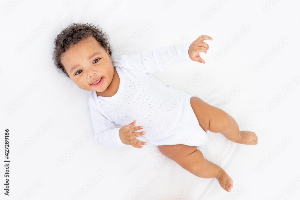 smiling African-American little baby on white bed in bedroom laughing smiling African-American little baby on white bed in bedroom laughing