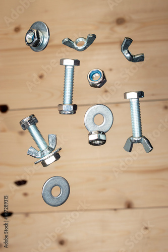 nuts, screws and washers are falling against the background of a light wooden board