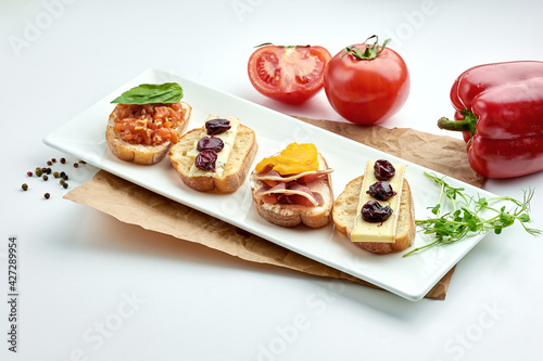 Appetizing italian antipasti - assorted bruschetta with salmon, cheese and jamon, served on a white plate on a white plate