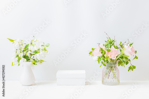 Empty white box and branches with pink tulips in a vase on a light background. Mockup banner for display of advertise product