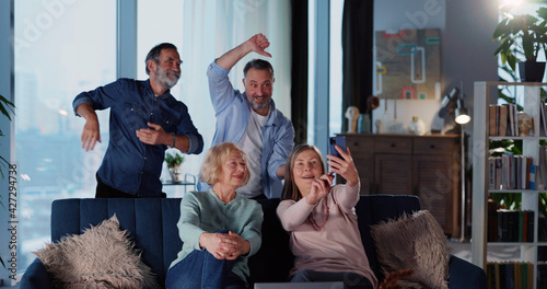 Joyful multi-generation family of two cheerul couples staying at home recording smartphone video having fun together on weekend. Relationships. photo