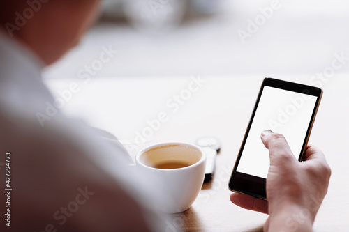 businessman hand holding a phone with isolated screen against moke up and drink coffee in the coffee shop blurred coffee cup background, Mock up concept