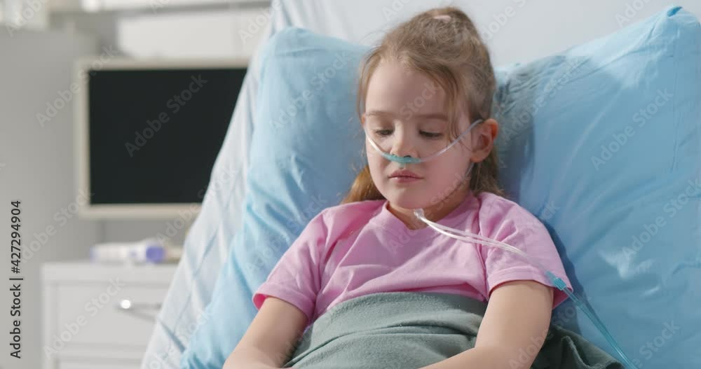 Girl suffering from pneumonia lying in hospital bed with oxygen nasal tube