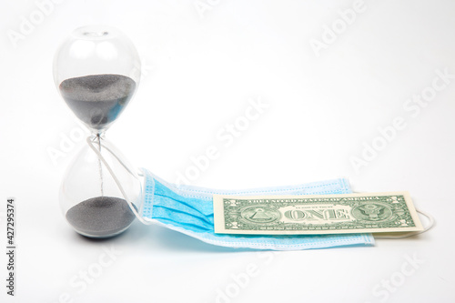 hourglass, dollar and medical mask on a white background. time and protection from the virus. financial losses due to the virus epidemic. business in medicine