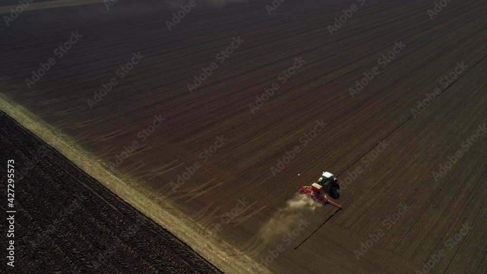 Aerial view from behind of a green tractor seeding, sowing agricultural crops at the field with dust behind Aerial view from behind of a green tractor seeding, sowing agricultural crops at the field with dust behind