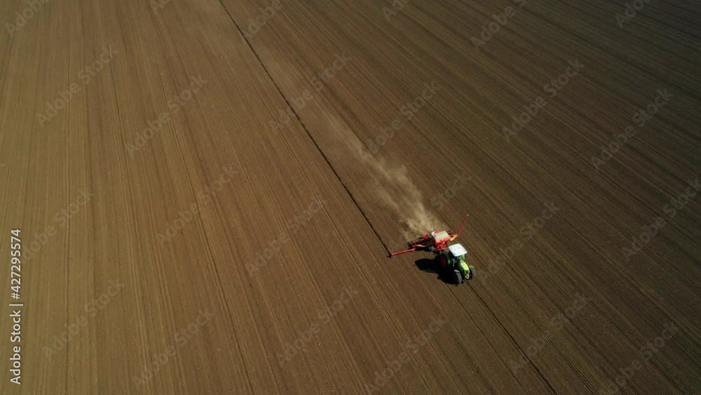 Aerial side view of a green tractor seeding, sowing agricultural crops at field Aerial side view of a green tractor seeding, sowing agricultural crops at field