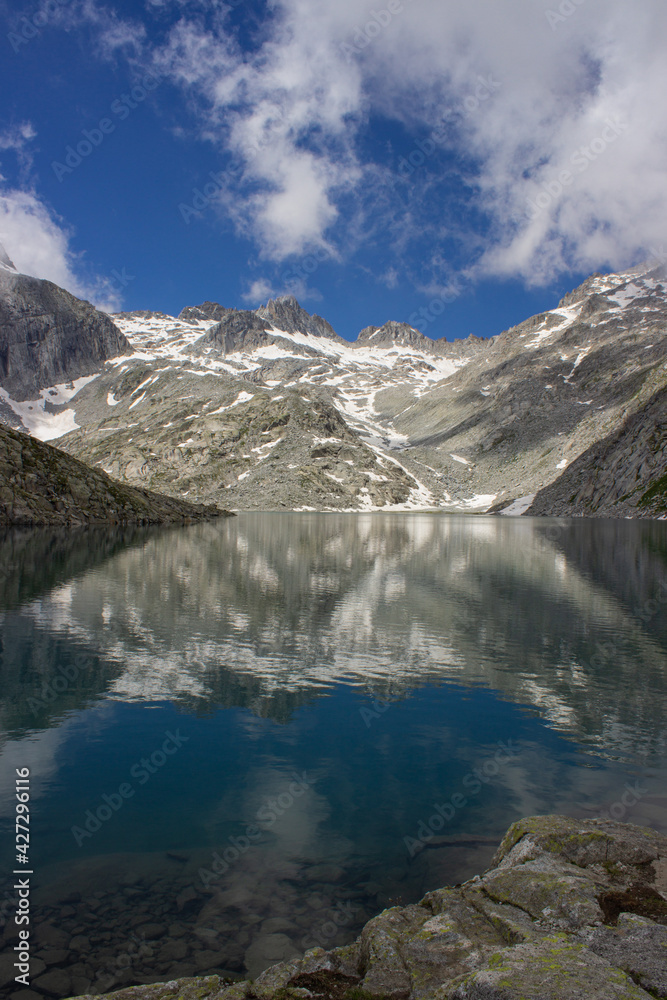 Lonely and austere Lake Vedretta at an altitude of 2600 meters. View of the high altitude lake framed by the mountains reflecting in the water. Adamello Brenta Natural Park, Italy. Vertical immage. Lonely and austere Lake Vedretta at an altitude of 2600 meters. View of the high altitude lake framed by the mountains reflecting in the water. Adamello Brenta Natural Park, Italy. Vertical immage.